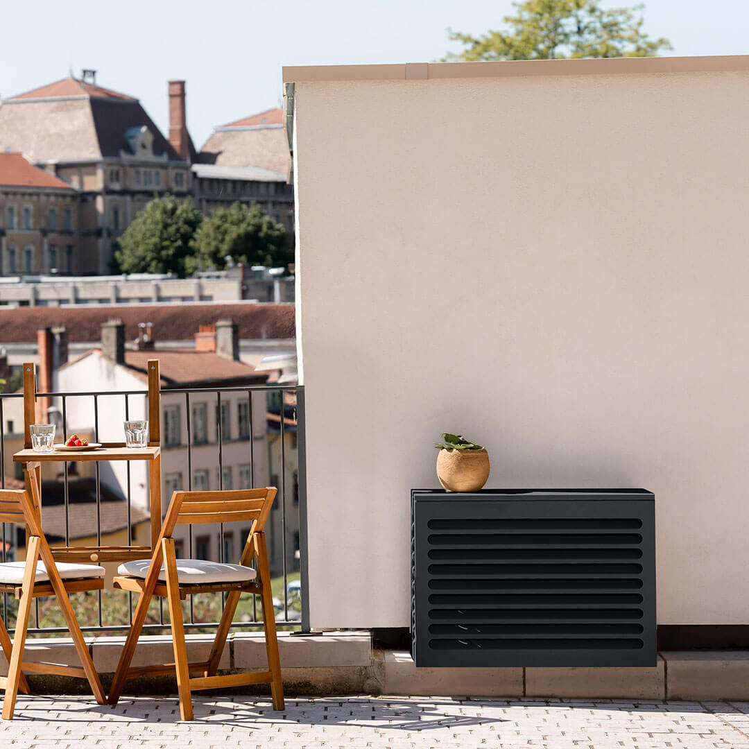 Pose de climatisation autorisée avec un cache clim de gris anthracite RAL7016 sur un balcon, installé contre un mur blanc, avec une vue urbaine en arrière-plan