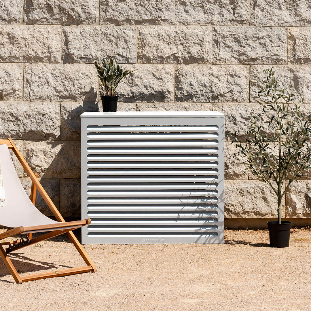 Cache clim blanc (RAL 9010) – , installé avec soin – vue de face avec déco. Structure ventilée et design, idéale pour sublimer une façade ou un jardin. Un rendu soigné qui allie déco et performance.